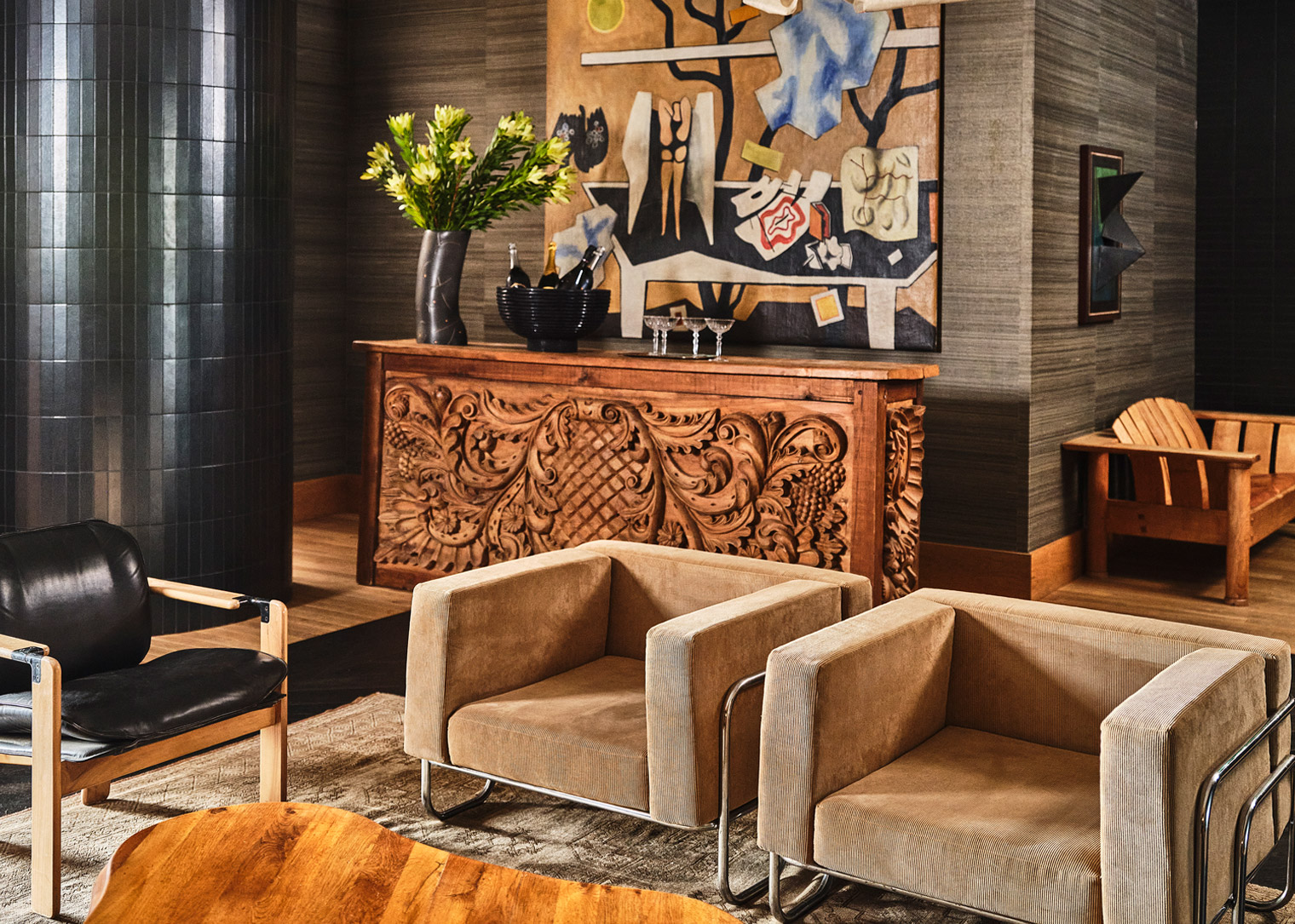 Cozy lounge with carved wood console, modern armchairs, and colorful artwork in quill room