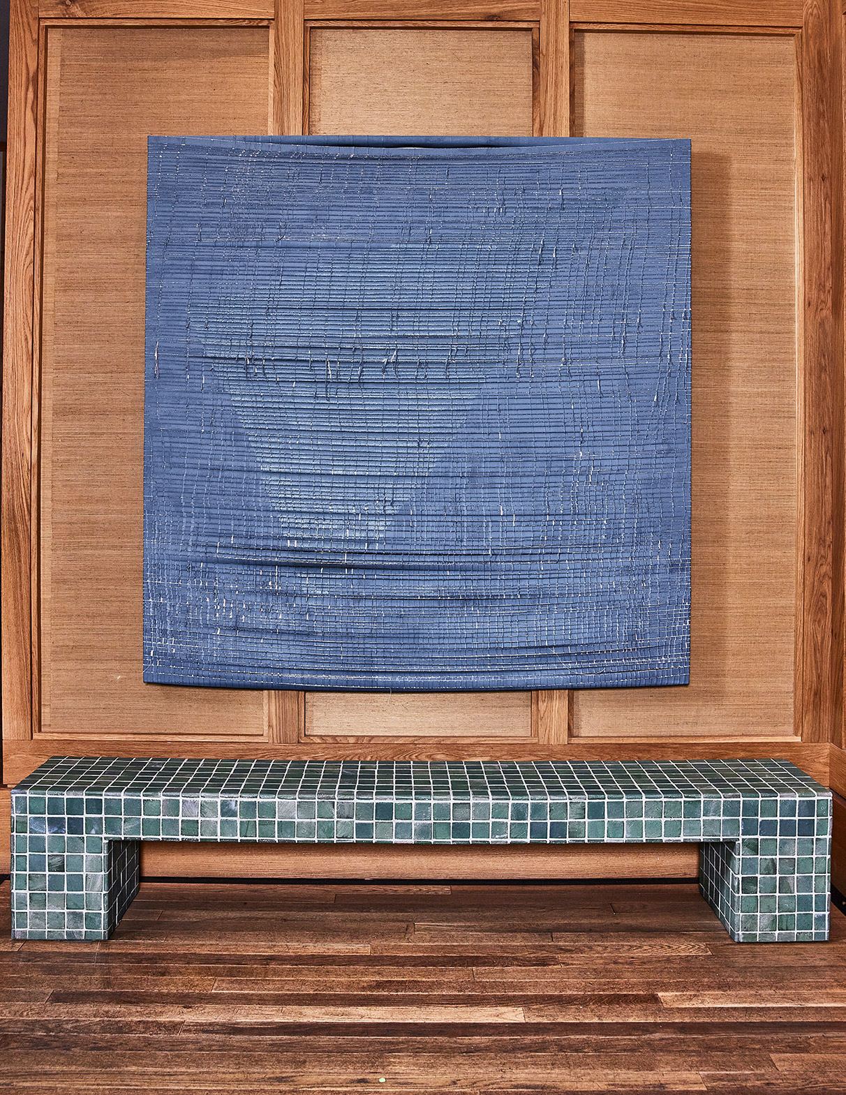 Textured blue wall hanging above a green tiled bench against wood-paneled wall