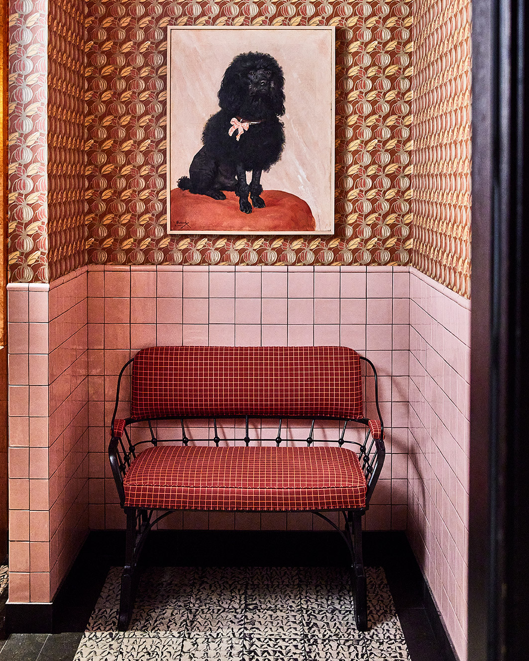 Red upholstered bench in tiled nook with patterned wallpaper and framed dog artwork