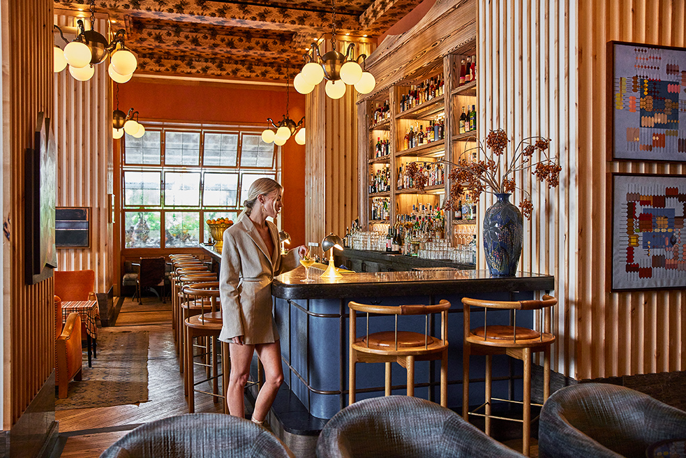 Woman at stylish bar with warm lighting, wood paneling, and backlit shelves