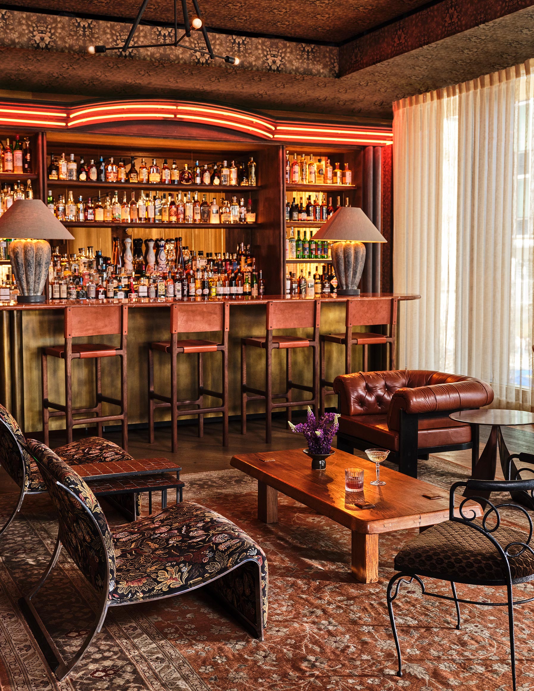 Cozy bar lounge with leather seating, patterned rugs, and backlit shelves of spirits