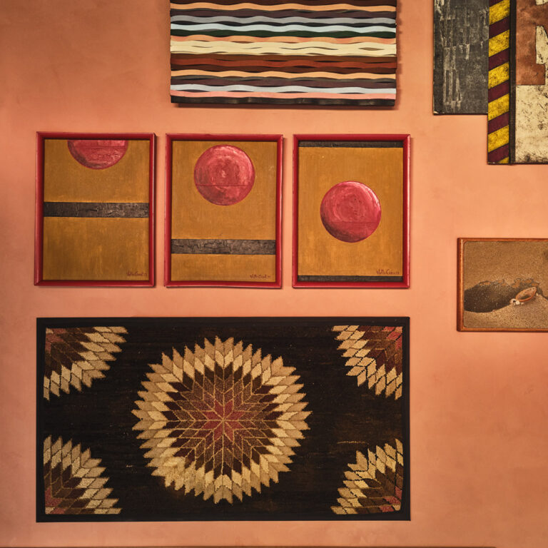 Gallery wall with abstract artwork and textiles in warm tones, featuring red circular motifs and geometric patterns