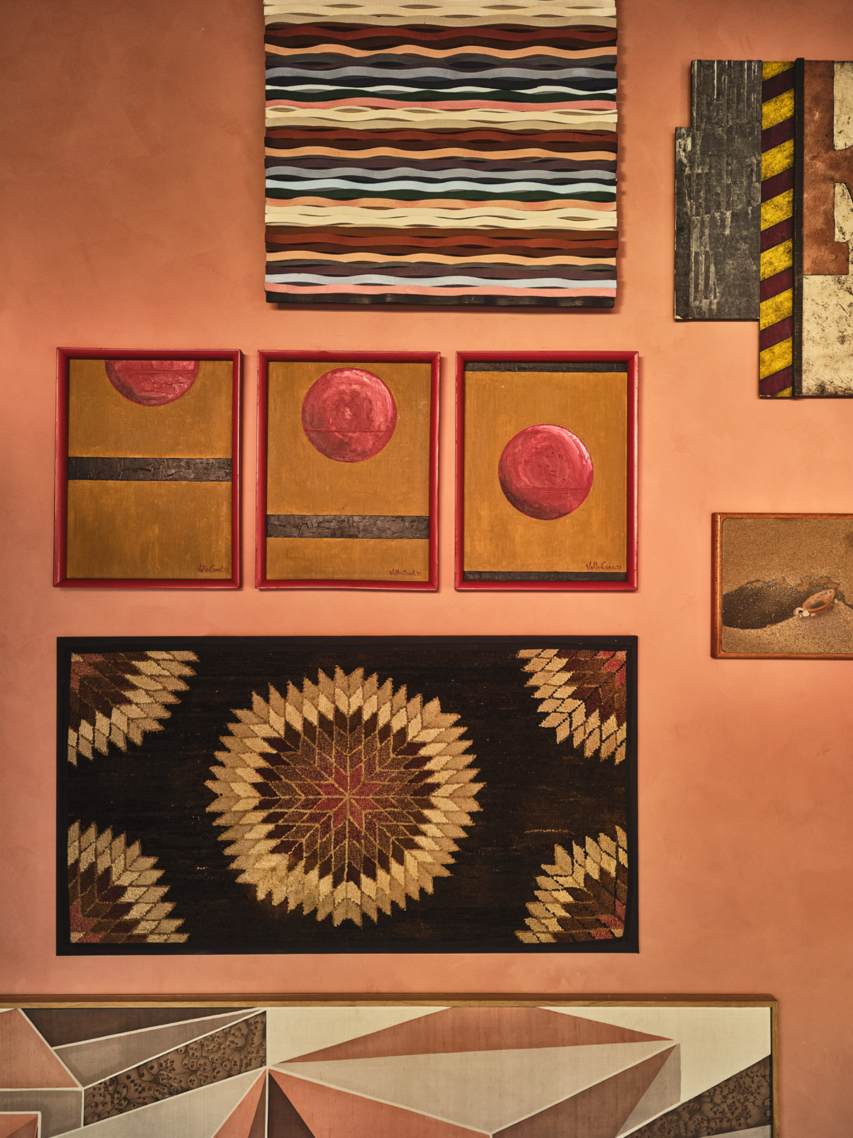 Gallery wall with abstract artwork and textiles in warm tones, featuring red circular motifs and geometric patterns