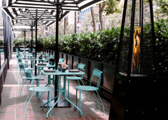Outdoor restaurant patio with striped umbrellas, café seating, and patio heaters