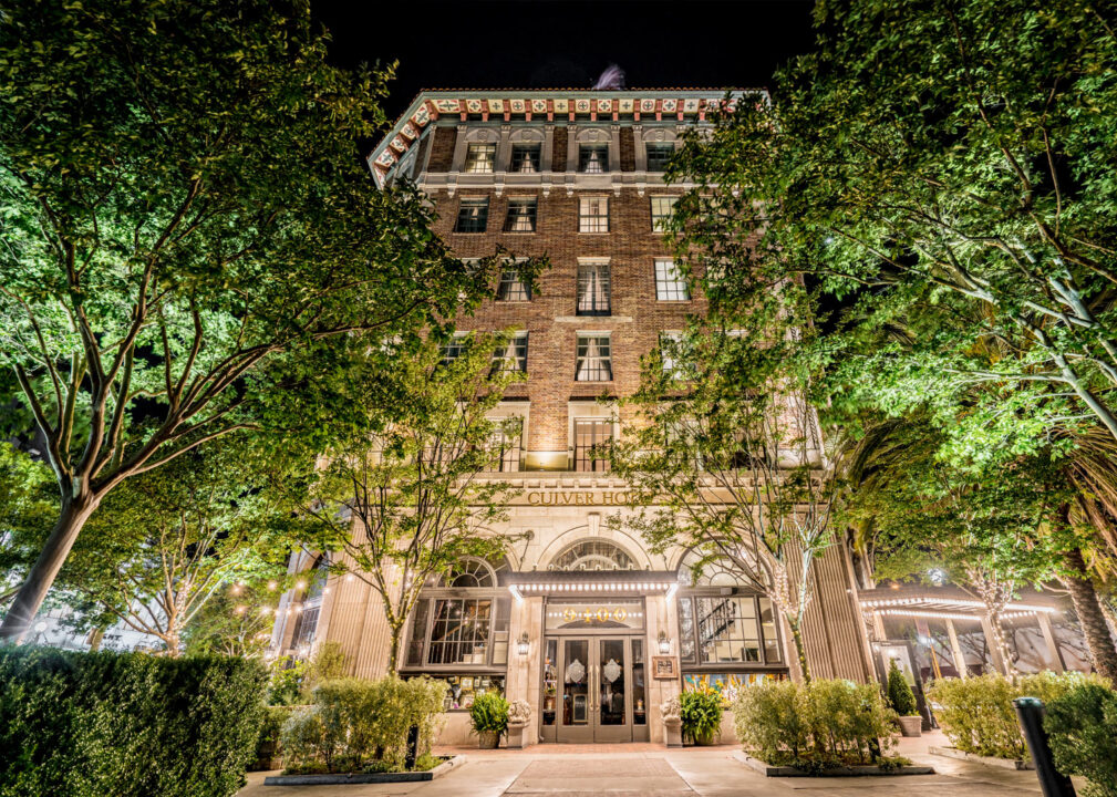 Historic hotel façade framed by trees, warmly lit at night.