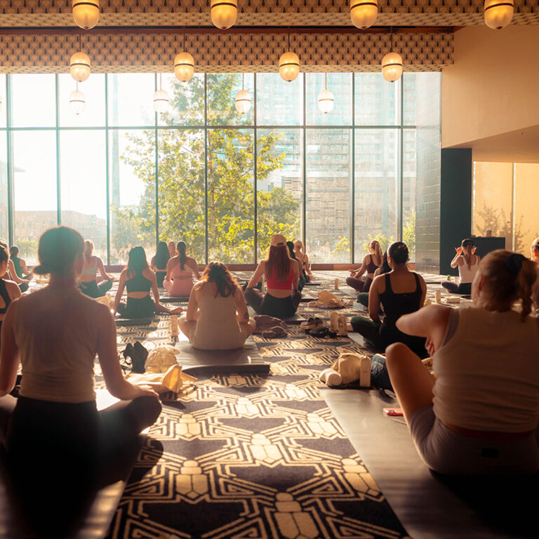 Group yoga in a sunlit studio with large windows and city views