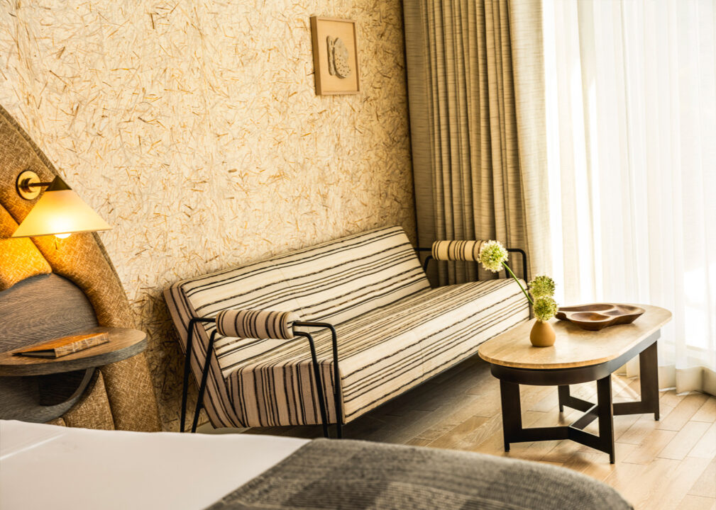 Sunlit hotel suite seating area with striped sofa, textured wallpaper, and modern wood coffee table