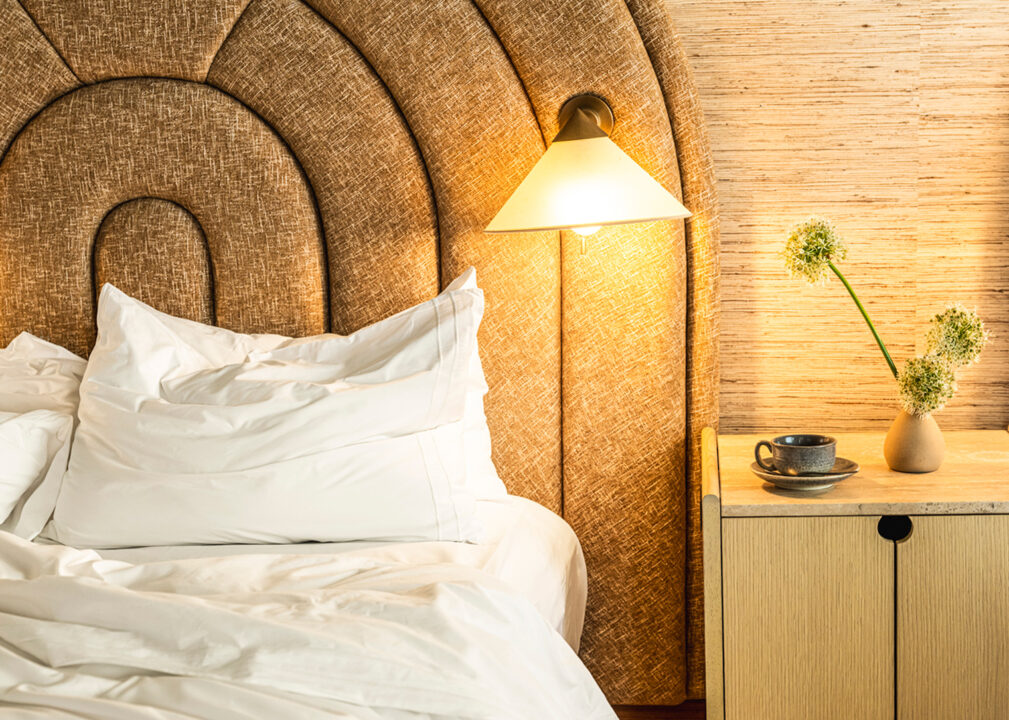 Close up of luxury hotel bed with textured headboard, bedside lamp, and modern nightstand decor