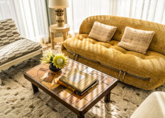 Stylish hotel suite lounge with curved sofa, vintage coffee table, and cozy sunlit seating area
