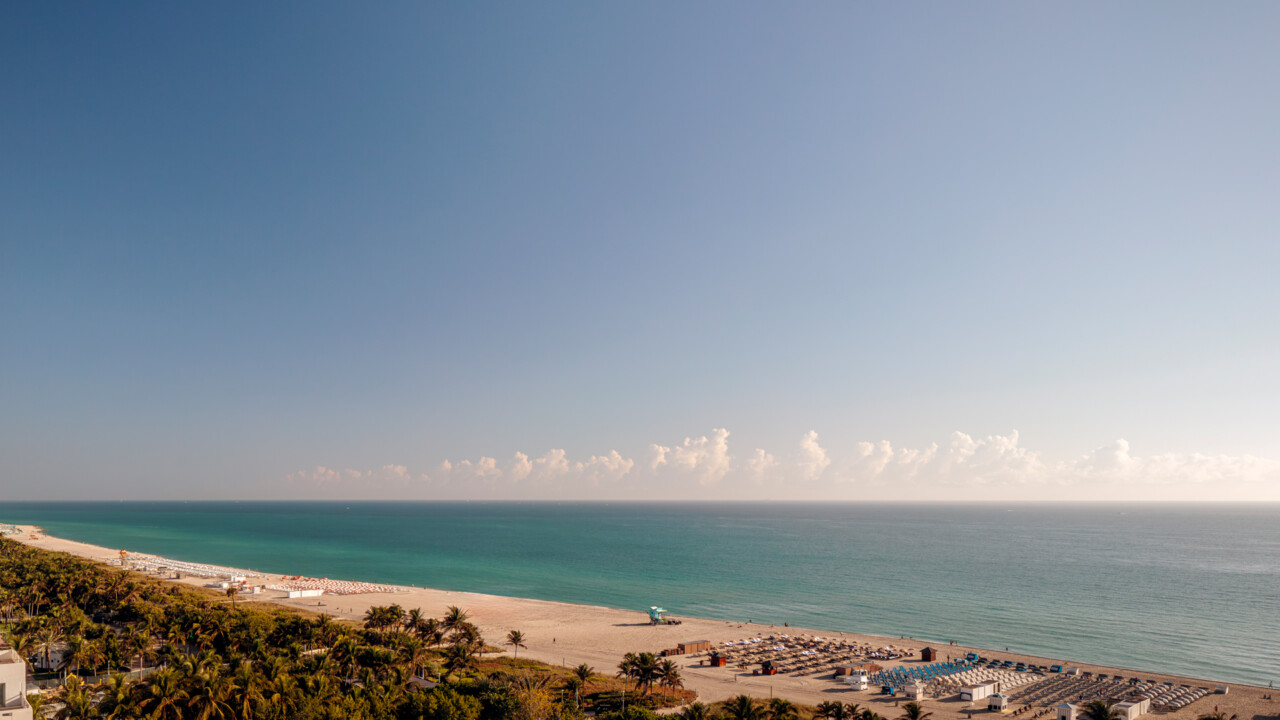 Expansive beachfront view with calm turquoise water, soft sands, and a wide open sky stretching to the horizon.