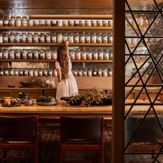 Woman reaching for jars of herbs on wooden shelves in a spa apothecary setting