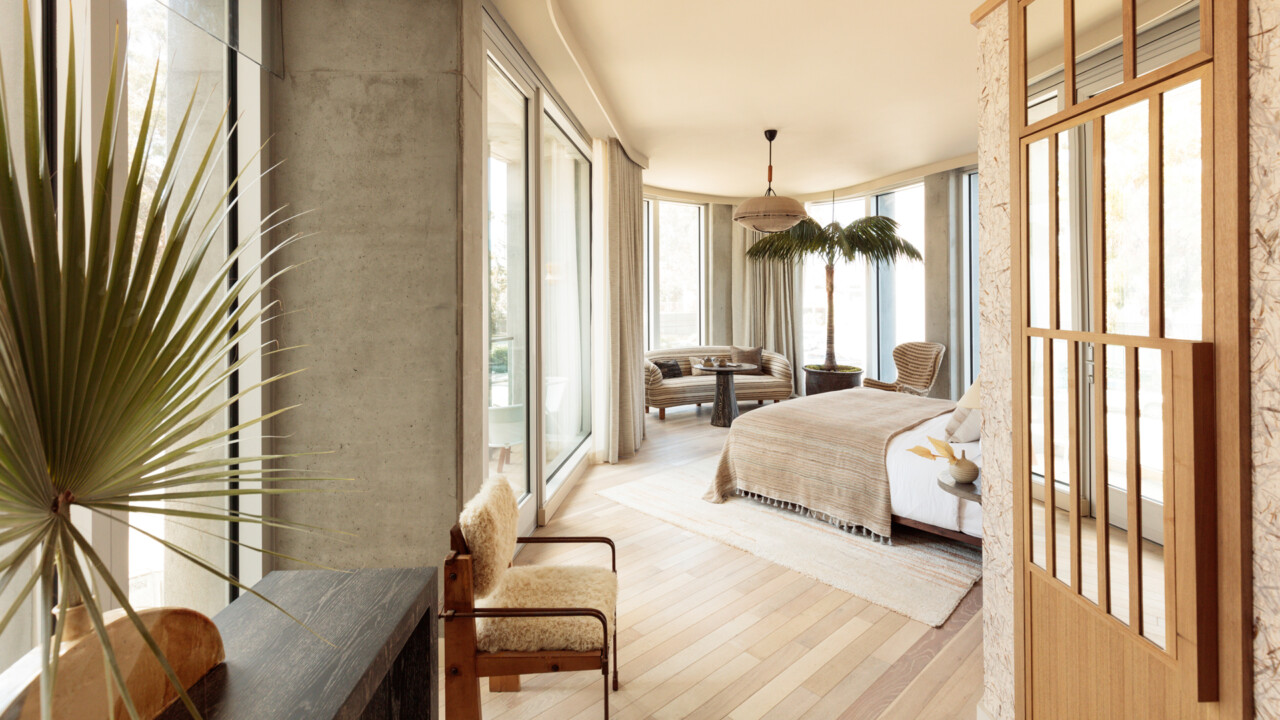 Sunlit luxury hotel suite with modern coastal design, floor-to-ceiling windows, and spacious seating area