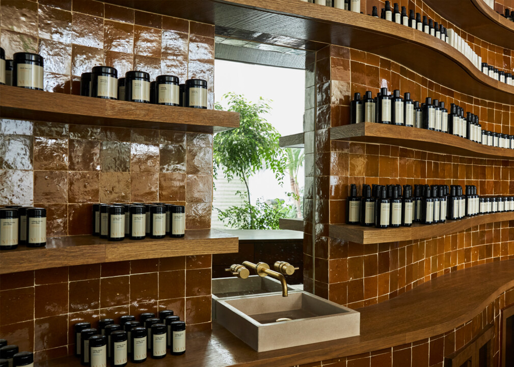 Spa apothecary shelves with curated wellness products and stone sink in warm tiled interior