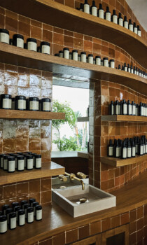 Spa apothecary shelves with curated wellness products and stone sink in warm tiled interior