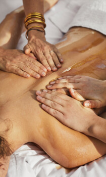Relaxing spa massage with multiple hands applying oil on back