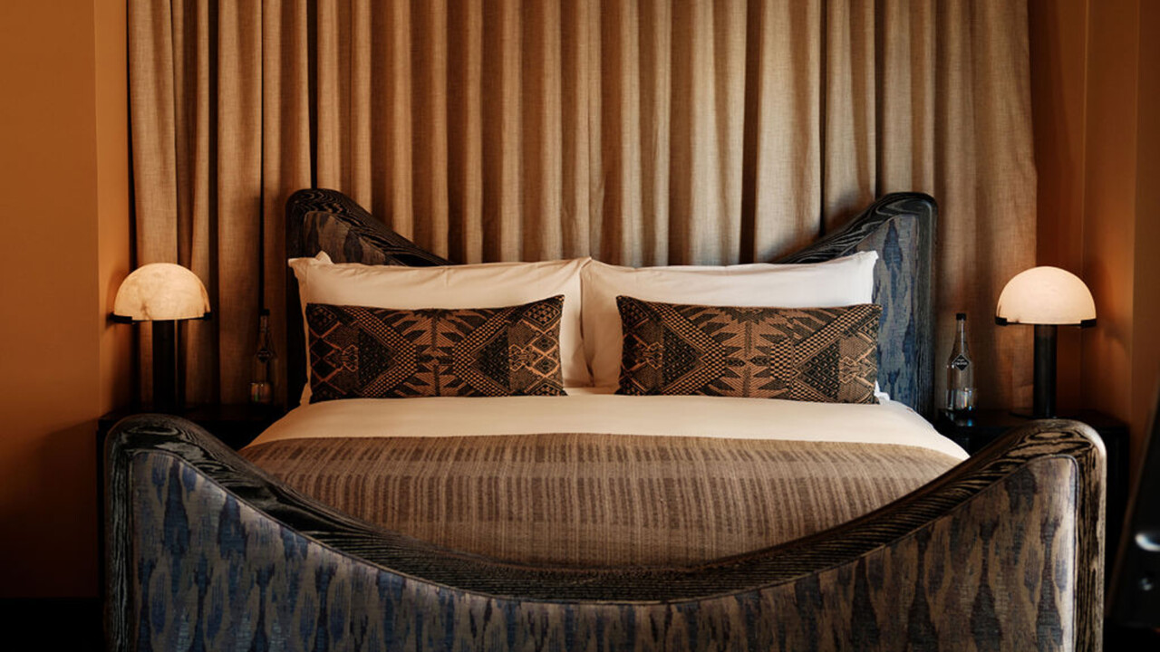 Moody, design-forward bedroom with sculptural bed, rich textures, and warm ambient lighting.