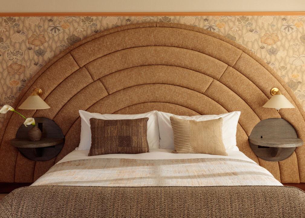 Stylish guest room at Santa Monica Proper Hotel with a large arched upholstered headboard, patterned wallpaper, neutral-toned bedding, and modern wall-mounted lamps with round bedside tables.
