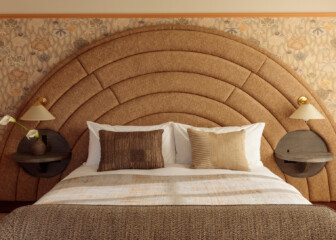 Stylish guest room at Santa Monica Proper Hotel with a large arched upholstered headboard, patterned wallpaper, neutral-toned bedding, and modern wall-mounted lamps with round bedside tables.