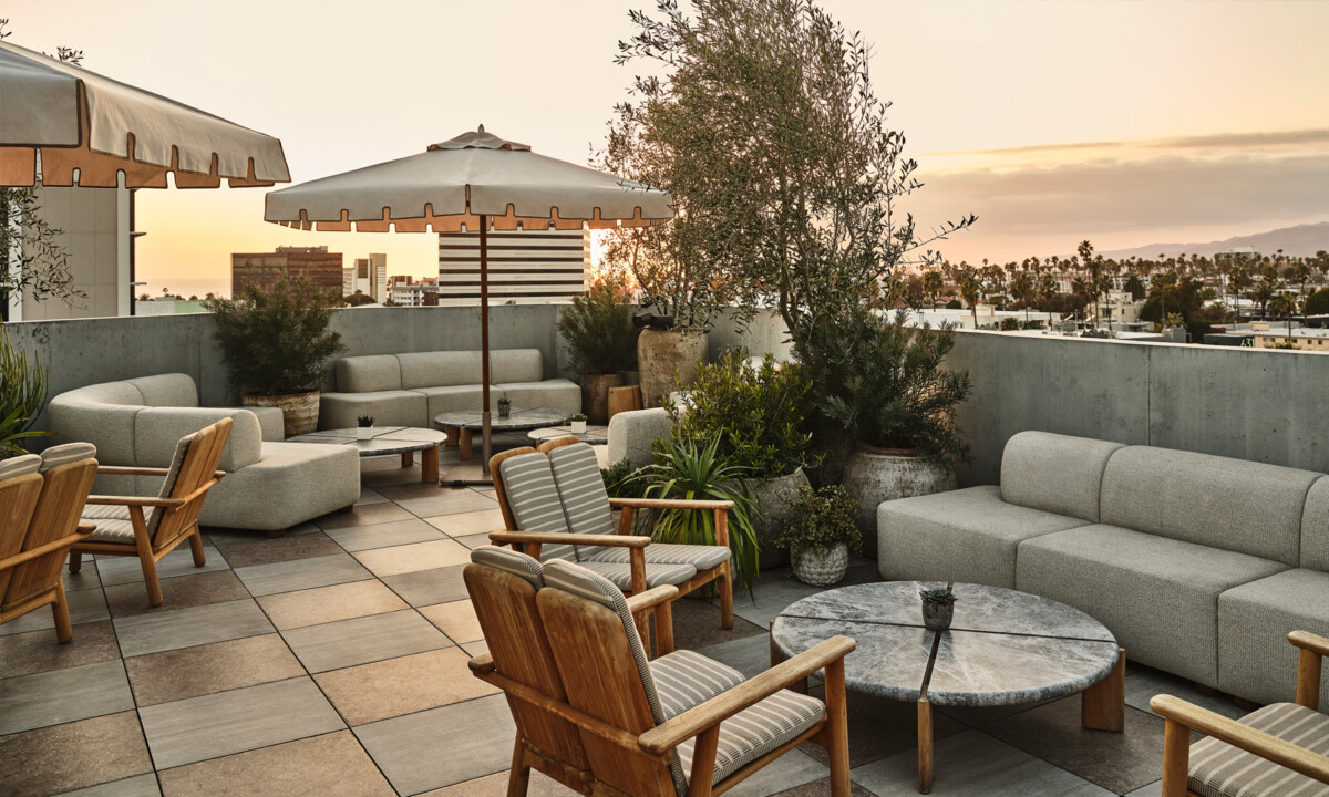 Rooftop terrace lounge with cushioned seating, umbrellas, and panoramic sunset views over Santa Monica