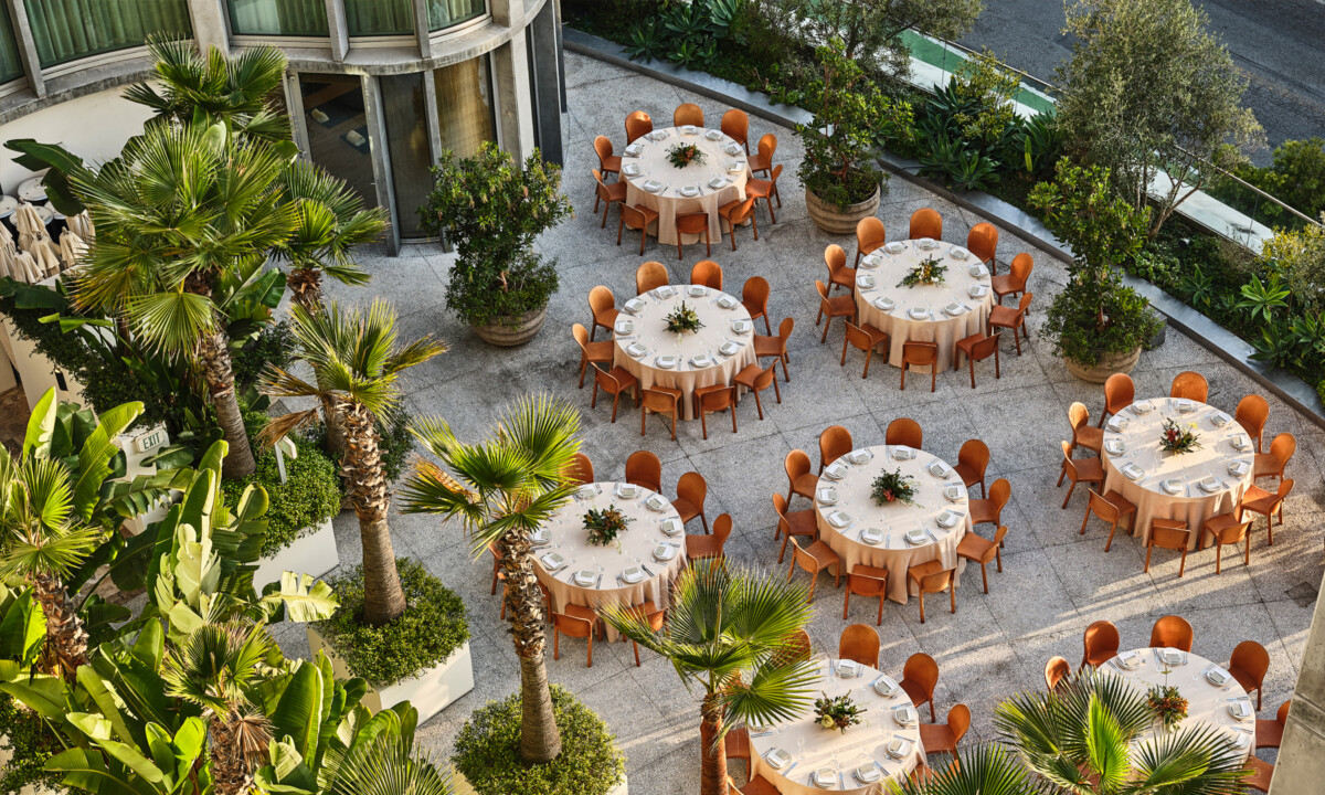 Outdoor courtyard event setup with round dining tables surrounded by palm trees and lush greenery