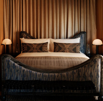 Moody, design-forward bedroom with sculptural bed, rich textures, and warm ambient lighting.