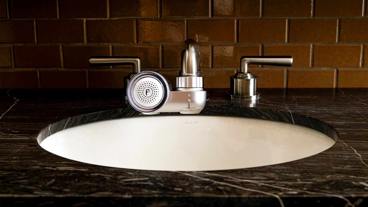 Modern bathroom sink with round faucet attachment and metallic handles, set against glossy brown tiled wall.