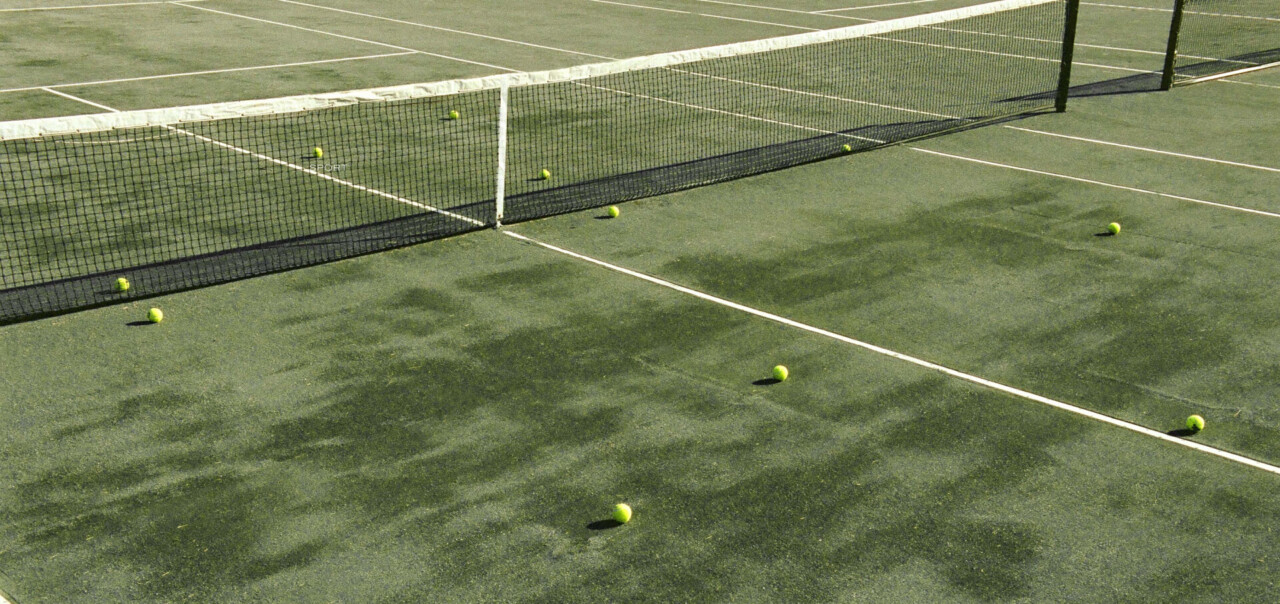 Tennis balls scattered across outdoor court by net