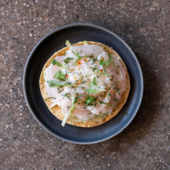 Fusion tostada with sashimi, herbs, and chili flakes, blending Mexican and Japanese flavors in a gourmet hotel dish.
