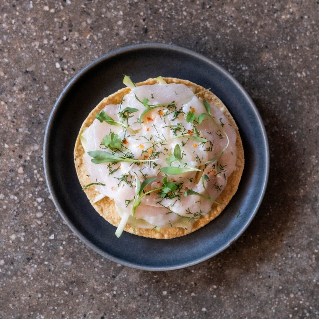 Fusion tostada with sashimi, herbs, and chili flakes, blending Mexican and Japanese flavors in a gourmet hotel dish.