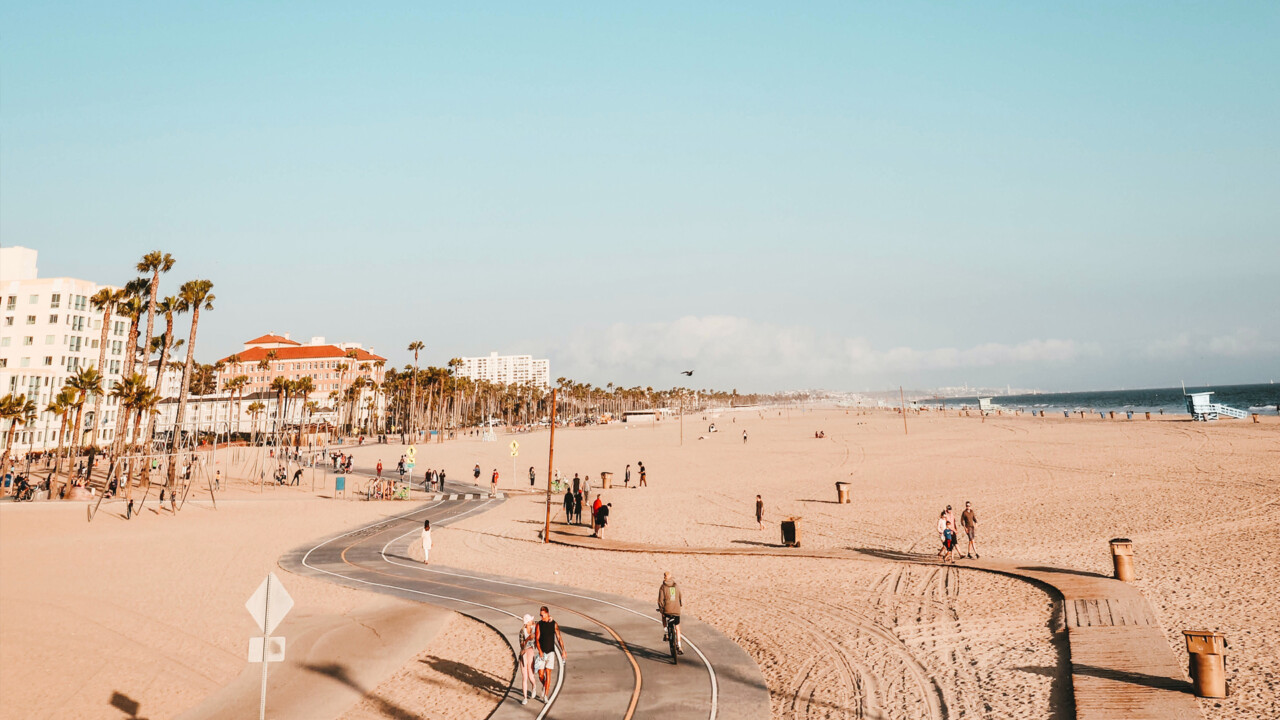 Sunny beachfront boardwalk with cyclists, palm trees, and ocean views
