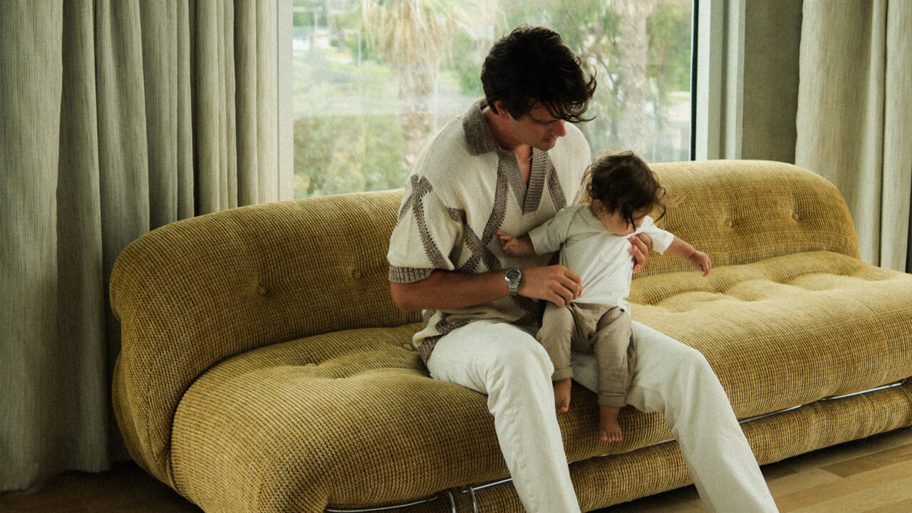 Man sitting on sofa holding a baby in a bright room