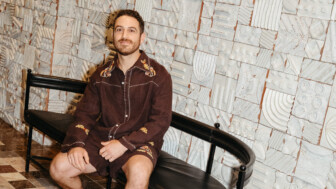 Man seated on black bench against geometric tile wall at Proper Hotel, with earth-toned flooring and artistic design.