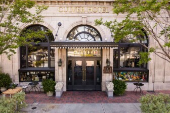 Historic Culver Hotel exterior with grand arched windows, black awning entrance, decorative columns, and leafy trees outside.
