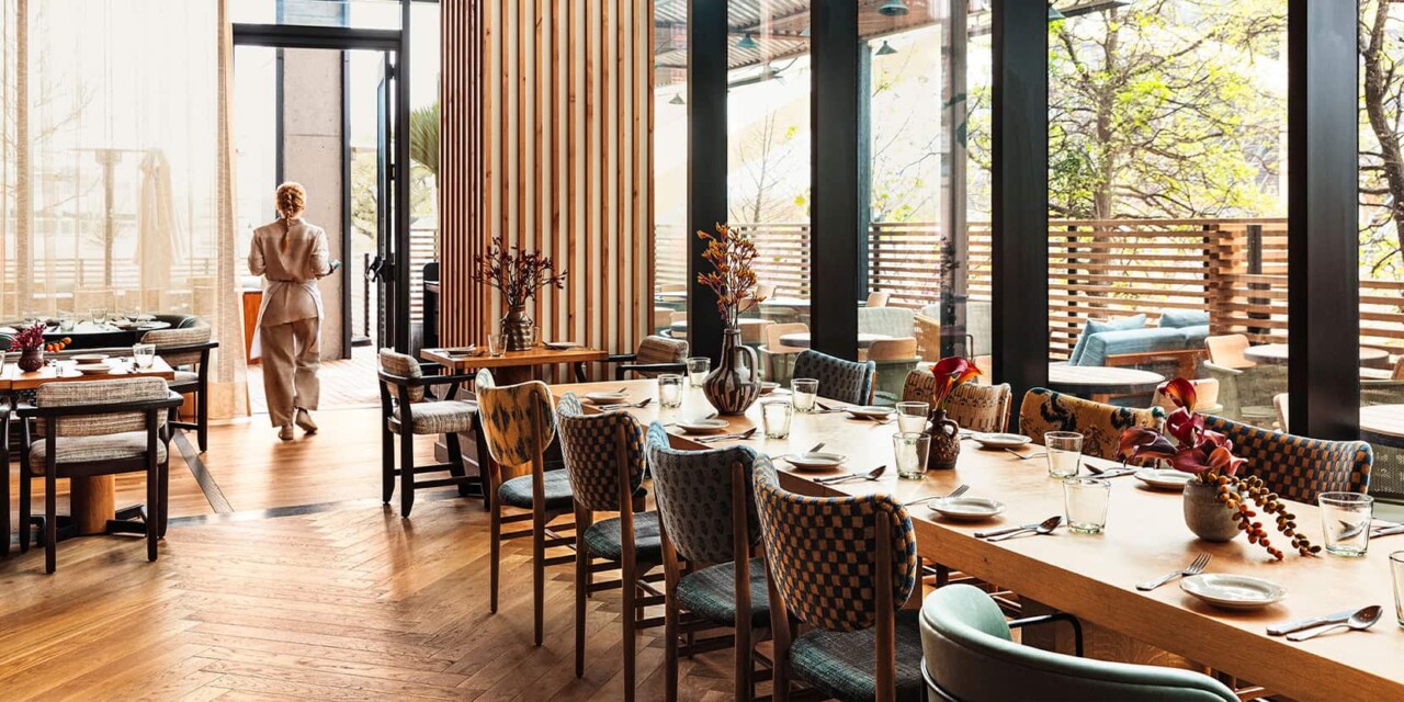 Eclectic dining room with round tables, padded chairs and various painted vases. A server walks by tables carrying a tray.
