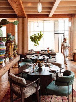 Eclectic dining room with round tables, padded chairs and various painted vases. A server walks by tables carrying a tray.