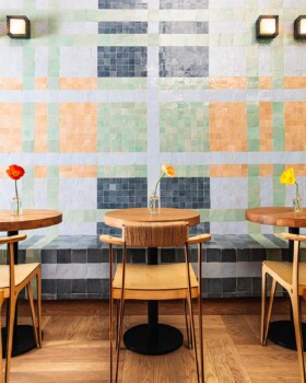 Café interior with wood tables, woven chairs, and pastel tile wall. Minimalist, warm, and colorfully inviting.