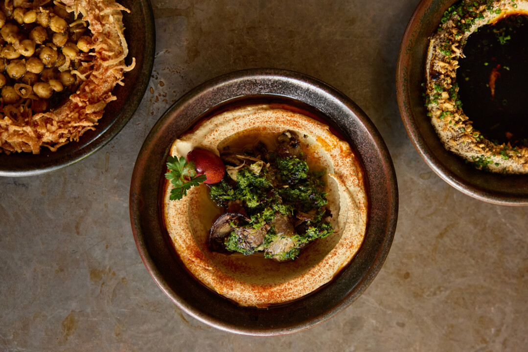 Assorted dishes including hummus with herbs, crispy chickpeas, and a savory dip served in ceramic bowls