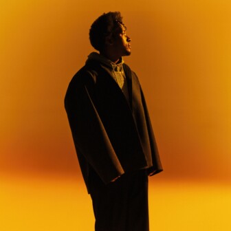 Person standing in warm golden light, looking upward with a calm, contemplative expression.