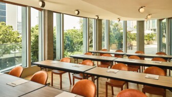 Bright classroom or seminar room with rows of tan chairs, tables, and large windows.
