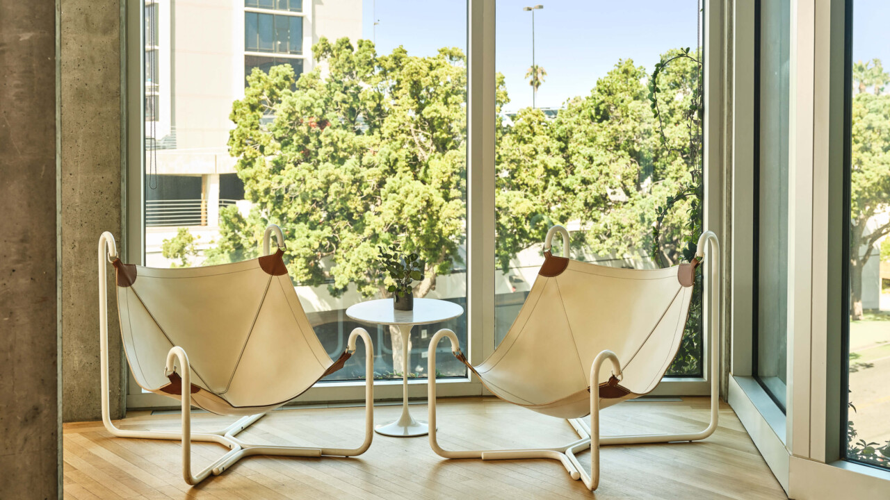 Two modern white lounge chairs facing window with outdoor trees and a round table.