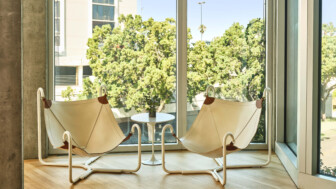 Two modern white lounge chairs facing window with outdoor trees and a round table.