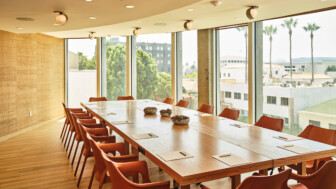 Bright conference room with long wooden table, orange chairs, and large city-view windows.