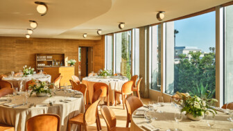 Bright event room with round tables, floral centerpieces, and large windows overlooking trees.