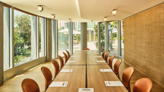 Bright meeting room with long wooden table, leather chairs, and expansive garden-facing windows.