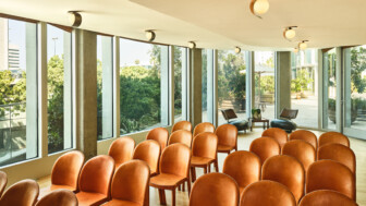 Rows of tan chairs in a sunlit conference or meeting room with large windows.