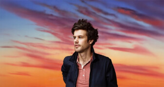 Person with blurred face standing in front of colorful sunset sky.