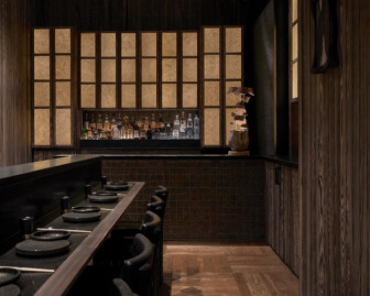 Intimate wood-clad bar and dining space with minimalist place settings and softly lit back bar
