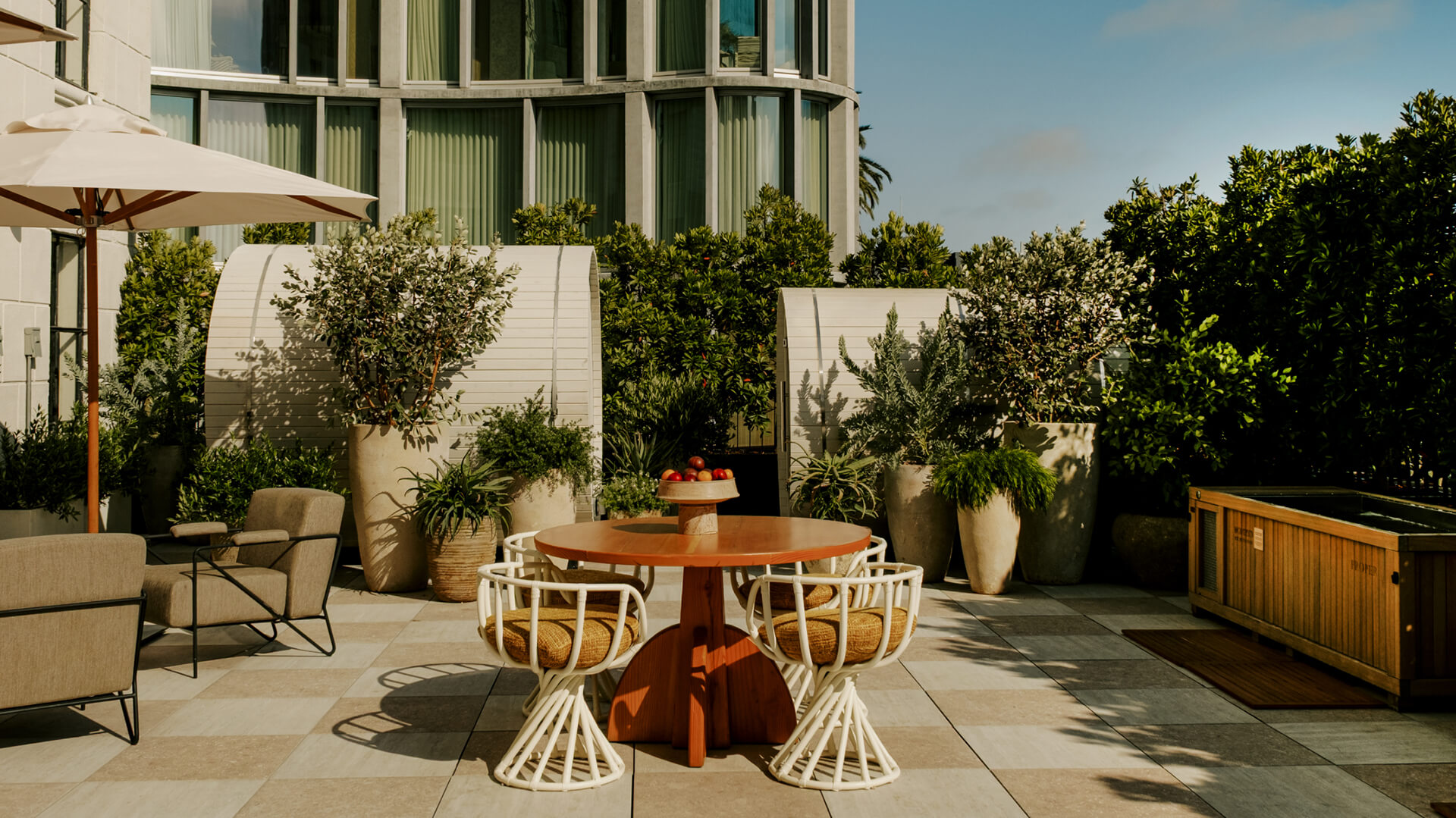 Outdoor patio with a round dining table, chairs, and plants in front of a building