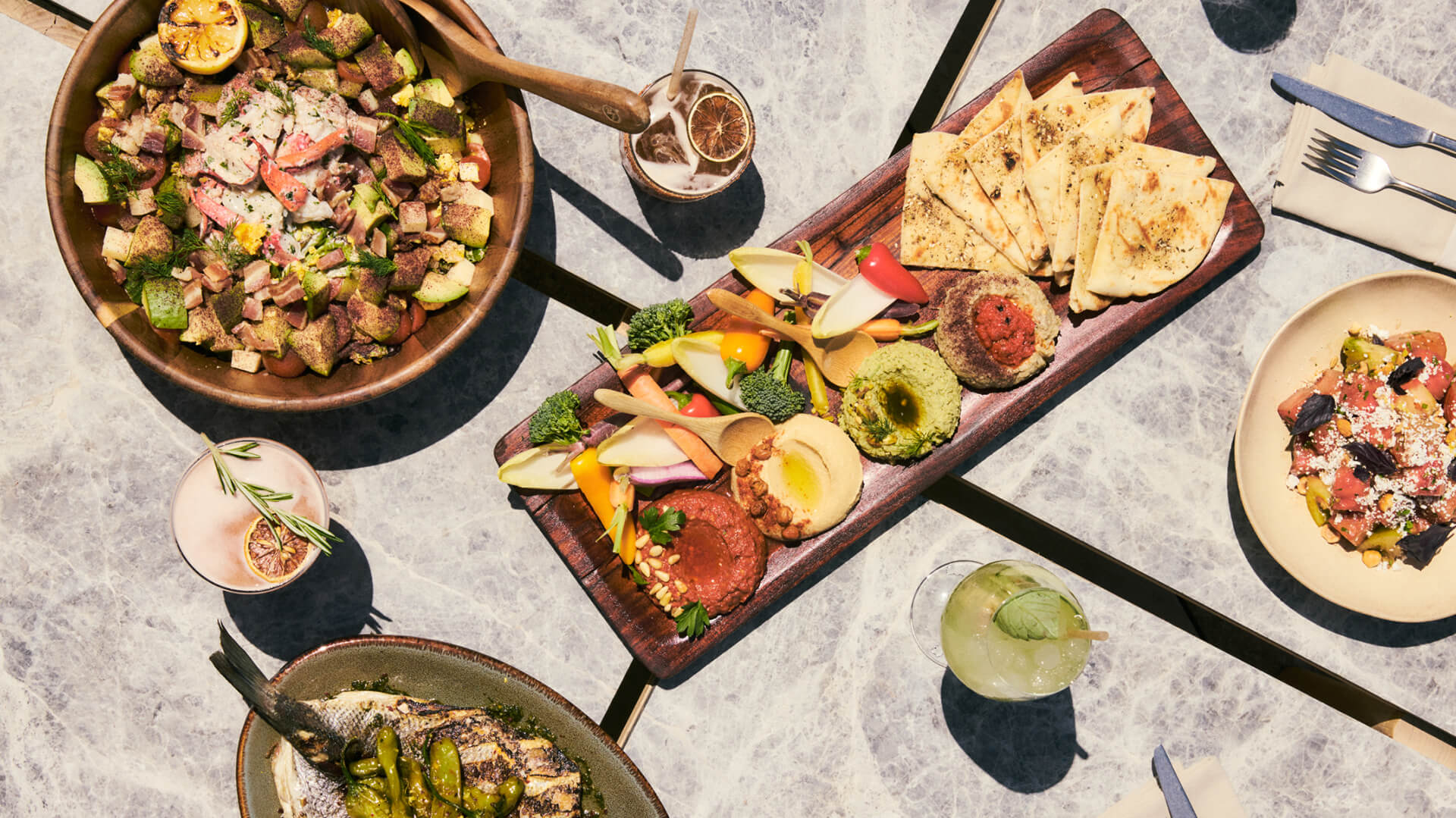 Overhead view of table with salad bowl, flatbread, dips, vegetables, and drinks