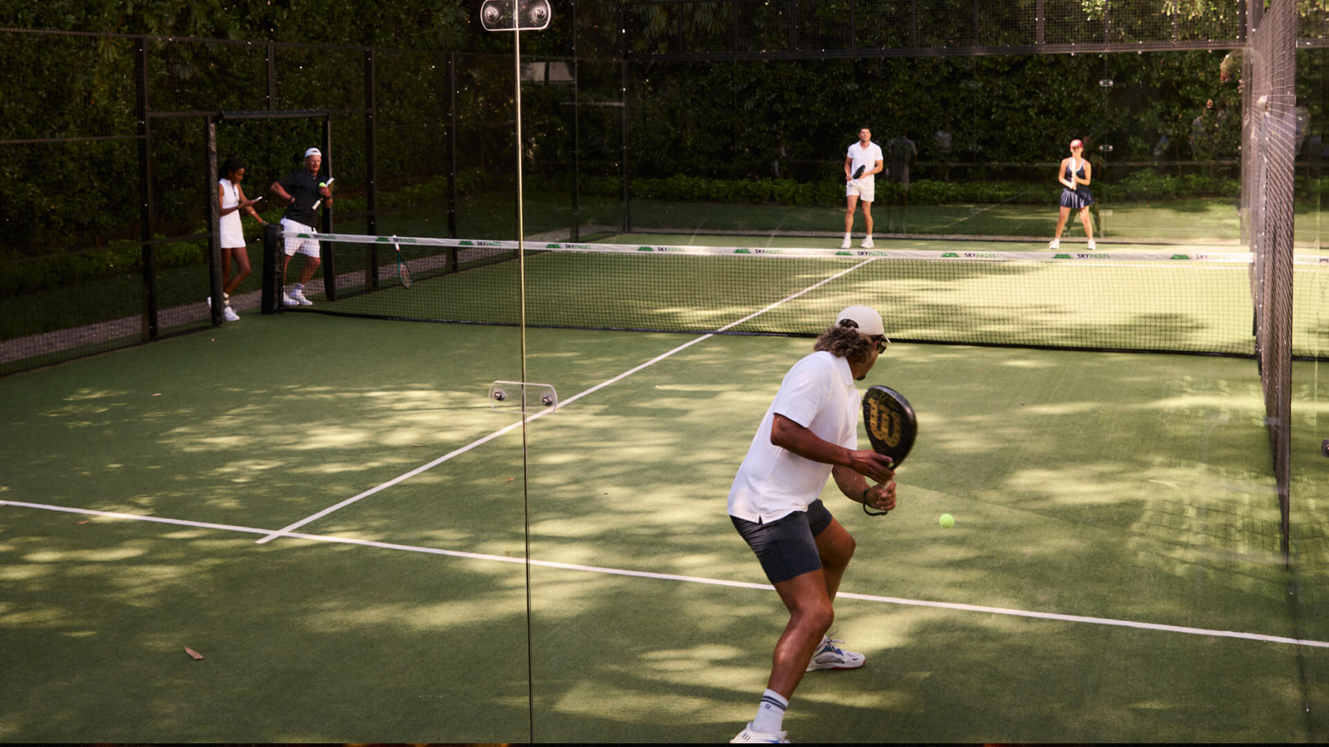Four people playing paddle tennis on a fenced outdoor court
